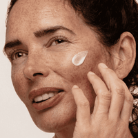 Gesicht einer Frau mit aufgetragener weißer Creme auf Wange und Fingerspitzen